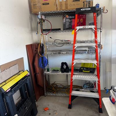 Werner red fiberglass A-frame stepladder, shown alongside a chrome wire shelving unit holding various tools, hardware organizers, and...