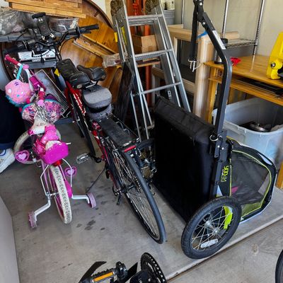 Assorted garage items including a pink child's bicycle with training wheels, a red adult bicycle, a black pet bike trailer, and an...