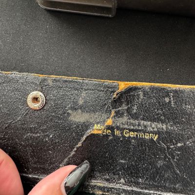 Sale Photo Thumbnail #56: Vintage black leather case showing significant wear and a gold-stamped "Made in Germany" mark near a metal snap closure.