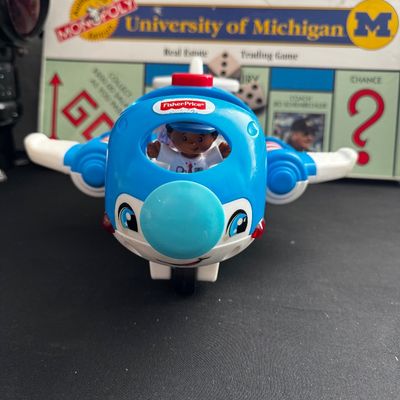 Sale Photo Thumbnail #45: Fisher-Price Little People Lil' Movers airplane toy with pilot figure, shown in front of a University of Michigan Monopoly board game.