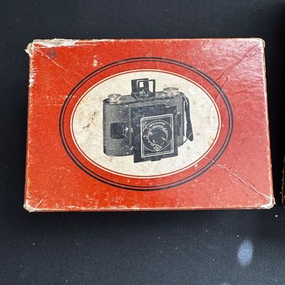 Sale Photo Thumbnail #67: Vintage red cardboard box for an Ansco Clipper camera, showing wear on the corners and edges.