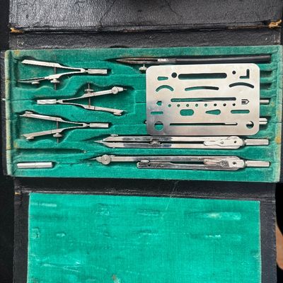 Sale Photo Thumbnail #55: Vintage German drafting tool set, featuring various metal compasses and an erasing shield housed in a green velvet-lined black leather case.