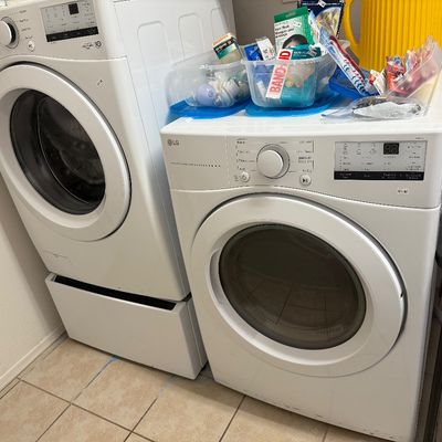 White LG front-loading washing machine on a pedestal base paired with a matching LG electric dryer.
