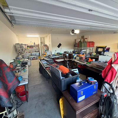 Garage packed with estate sale items, featuring tools, blue metal toolbox, storage totes, power tools, lawn gear, and household goods...