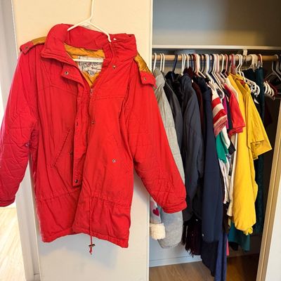 Vintage Profile by Nevica red insulated ski jacket with gold accents, hanging in a closet with other clothing.