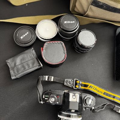 Sale Photo Thumbnail #5: Vintage Nikon SLR film camera body with attached lens, yellow and black Nikon strap, three additional lenses, filters, and a canvas camera bag.
