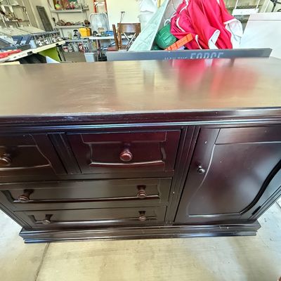 Dark espresso wooden dresser featuring multiple drawers, a cabinet door, and decorative trim, shown stored in a garage setting.