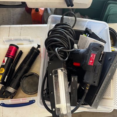 Assorted workshop tools and electronics, including a handheld work light, an Easypower heat gun, and a grease gun in a separate container.