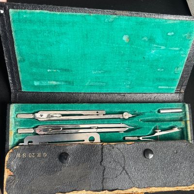 Sale Photo Thumbnail #54: Vintage drafting tool set in a worn black case with a green velvet-lined interior, featuring various metal compasses and dividers.