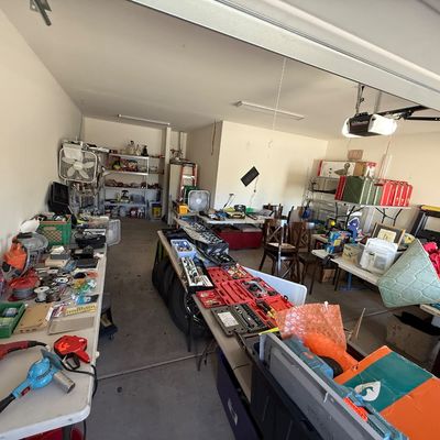 Garage filled with various items for sale, including power tools, hand tool sets, automotive supplies, and household goods arranged on...