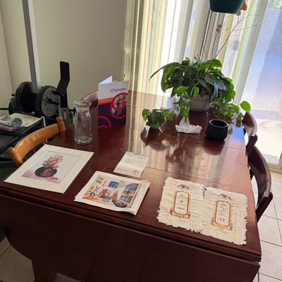 Dark wood drop-leaf dining table set with assorted artwork prints, glass vases, and potted plants.