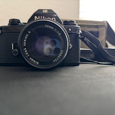 Sale Photo Thumbnail #2: Vintage Nikon EM 35mm SLR film camera equipped with a Nikon Series E 50mm f/1.8 lens and a black neck strap.