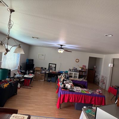 Wide view of an estate sale setup inside a home, featuring folding tables draped in cloth and displaying various household items, toys,...