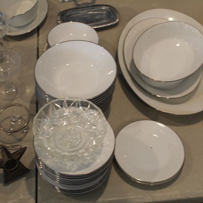 Assorted white porcelain dinnerware with silver rims, including plates, bowls, and platters, shown alongside cut glass bowls and stemware.