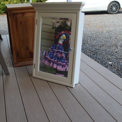 Sale Photo Thumbnail #37: White wooden medicine cabinet with a mirrored door and crown molding detail, shown sitting on a deck.