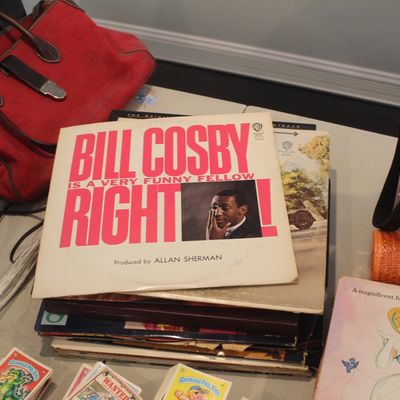 A stack of vintage vinyl records featuring Bill Cosby's "Is a Very Funny Fellow, Right!" album on top, displayed alongside...