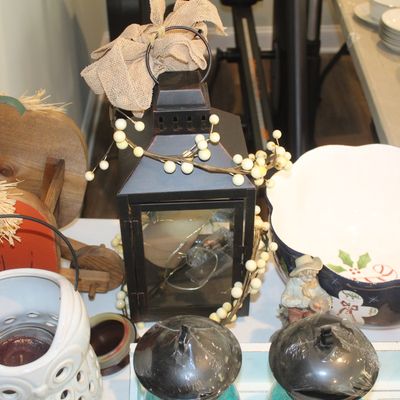 Assorted seasonal home decor, including a black metal lantern with a burlap bow, a festive holiday serving bowl, and rustic wooden...