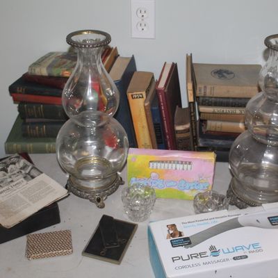 Pair of vintage clear glass hurricane lamp bases with ornate metal feet, displayed alongside a collection of vintage books, a Pure Wave...