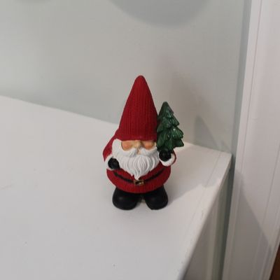 Sale Photo Thumbnail #10: Small Christmas gnome figurine wearing a red hat and holding a miniature evergreen tree, displayed on a white shelf.