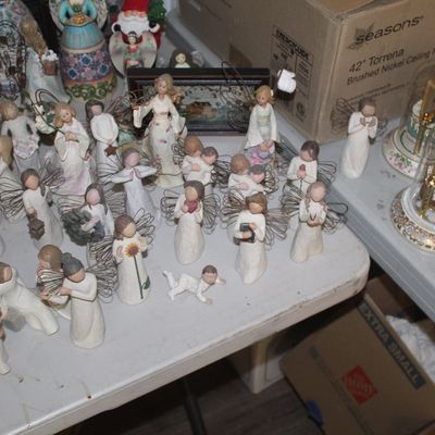 Large collection of Willow Tree angel and family figurines, displayed alongside decorative dome clocks on a folding table.