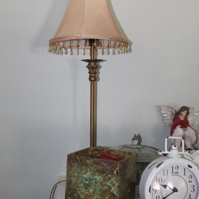 Vintage brass buffet lamp with a beaded fringe shade, displayed alongside a white distressed alarm clock and a textured square planter.