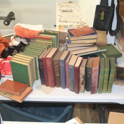 A collection of vintage books, including hymnals and matching green-bound volumes, displayed on a folding table alongside clothing and...