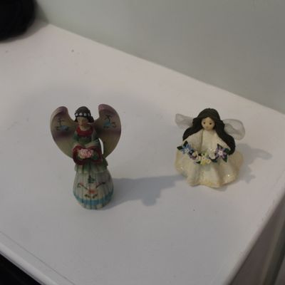 Sale Photo Thumbnail #11: Two small decorative angel figurines, one in a green dress with painted wings and the other in a white dress holding a flower garland.