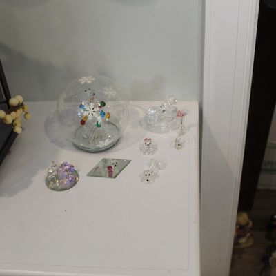 Sale Photo Thumbnail #39: Collection of small glass and crystal figurines, including a snow globe with a snowflake motif and miniature animal figures, displayed on a white surface.