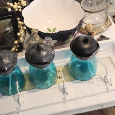 Assorted home decor items including a trio of blue glass solar lights on a white wooden hook rack, a festive holiday bowl, and a black...