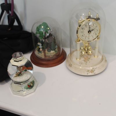 Sale Photo Thumbnail #23: Vintage anniversary clock with a glass dome and floral base, displayed alongside a small decorative snow globe and a miniature garden scene under a glass cloche.