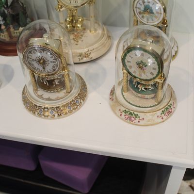 Sale Photo Thumbnail #25: Collection of vintage miniature carousel clocks under glass domes, featuring ornate porcelain bases with gold accents and floral motifs.