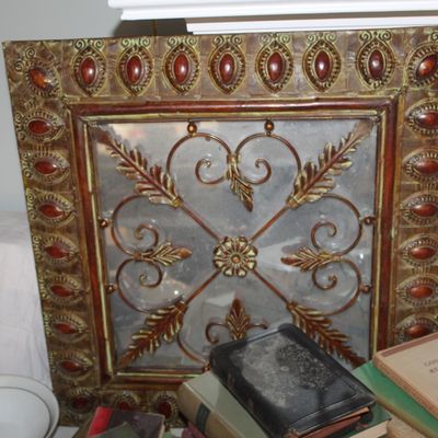 Ornate square wall mirror featuring a decorative metal frame with red cabochon accents and a central wrought-iron style overlay.