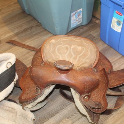 Sale Photo Thumbnail #44: Vintage leather Western horse saddle with floral tooling and a padded seat, shown alongside a fleece-lined girth strap.