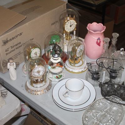 Assorted tabletop decor including glass-domed anniversary clocks, Willow Tree angel figurines, cut glass tableware, and a pink ceramic vase.