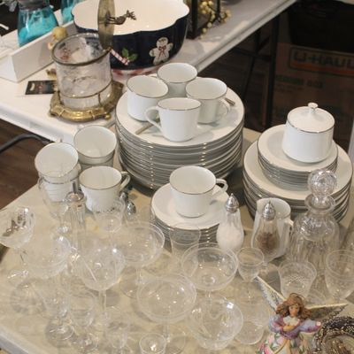 Vintage white porcelain dinnerware set with silver trim, accompanied by an assortment of cut crystal glassware, decanters, and a pitcher.
