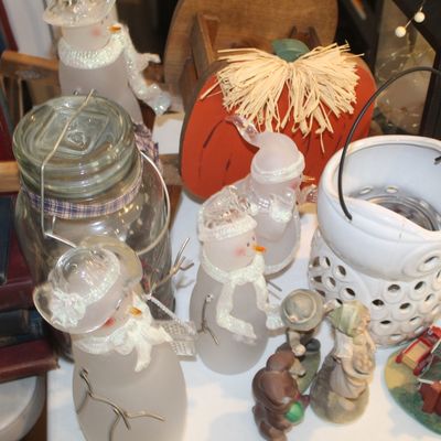 Assortment of seasonal home decor, including frosted glass snowman figurines, a wooden pumpkin, a white ceramic lantern, and vintage books.