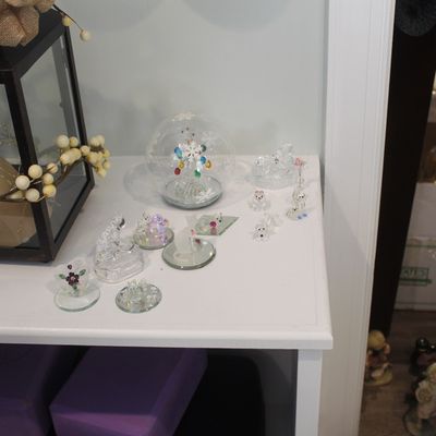 Sale Photo Thumbnail #40: Collection of small glass and crystal figurines, including a snow globe, animals, and floral motifs, displayed on a white shelf alongside a decorative lantern.