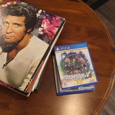 A stack of vinyl records featuring Tom Jones alongside a small stack of PlayStation 4 video games, including Danganronpa V3: Killing...