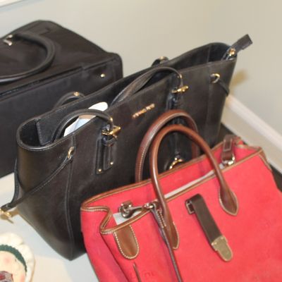 Collection of designer handbags, including a red fabric tote with brown leather trim and two black leather shoulder bags.
