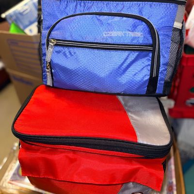 Two soft-sided cooler bags, including a blue Ozark Trail cooler and a red and grey insulated lunch bag.