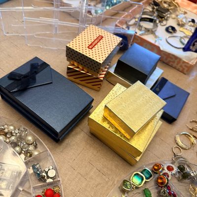 Assorted jewelry gift boxes, including Liz Claiborne and gold foil styles, displayed alongside trays of costume jewelry.