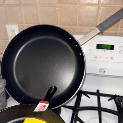 Large nonstick commercial-style skillet with a silicone handle sleeve, shown alongside new Lodge cast iron cookware.