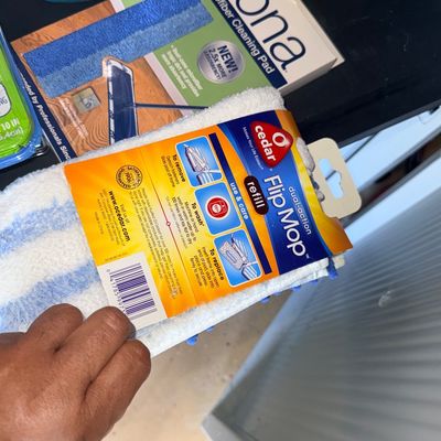 O-Cedar dual-action Flip Mop refill pad in original packaging, alongside additional household cleaning supplies like a Bona microfiber...