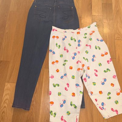 Two pairs of women's pants laid flat on a hardwood floor, including Seven7 dark-wash blue jeans and white crop pants featuring a...