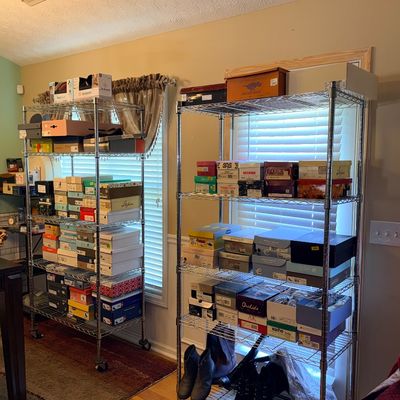 Two metal wire shelving units organized with stacked new shoe boxed and pairs of ankle boots on the bottom shelf.