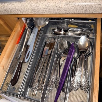Kitchen drawer containing metal mesh organizers filled with various stainless steel flatware and utensils.