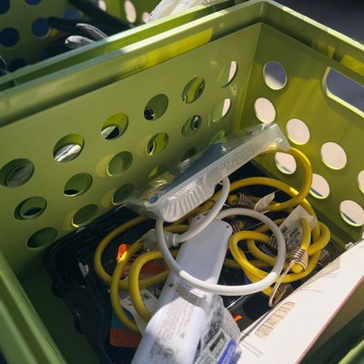 Lime green plastic storage crate filled with assorted hardware items, including yellow bungee cords and a white power strip.