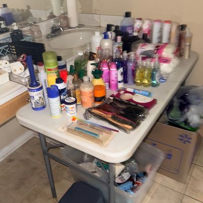 Large assortment of toiletries and personal care items arranged on a folding table in a bathroom, including shampoos, body washes, hair...