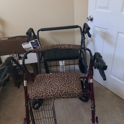 Burgundy four-wheel rollator walker with leopard-print cushioned seat and backrest, equipped with a lower wire storage basket.