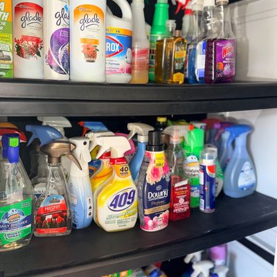 Black plastic utility shelving unit filled with various household cleaning supplies and laundry products.